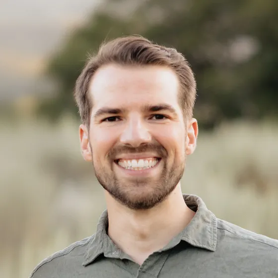 Ben Romney, smiling, outdoors in Utah with blurred green foothills behind him.